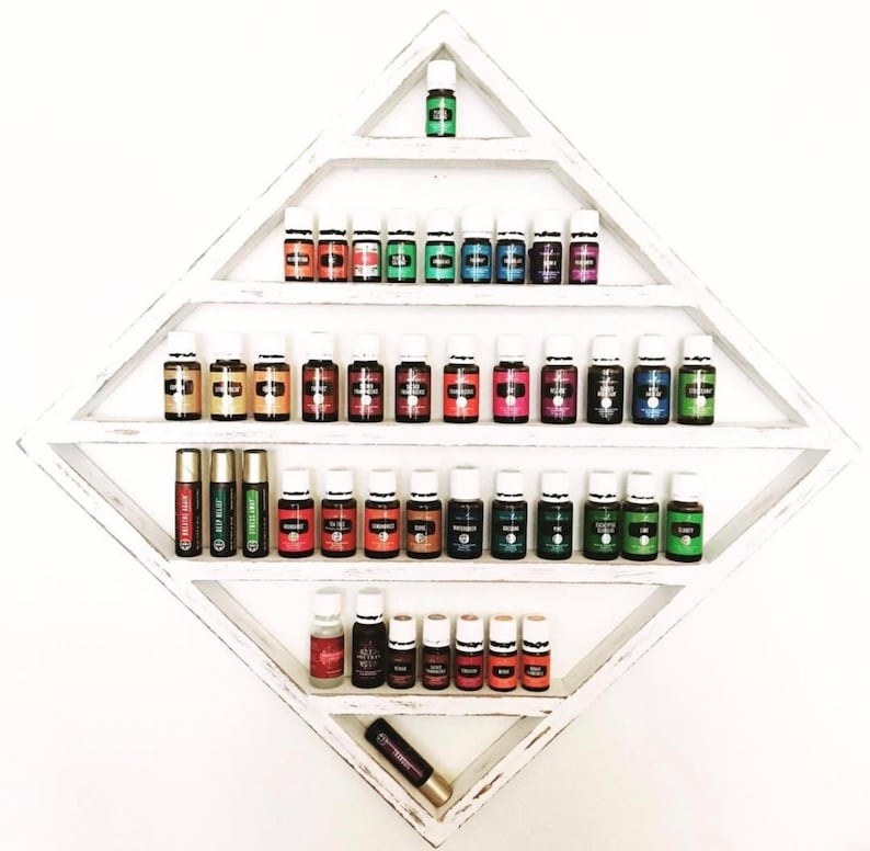 May include: A white diamond-shaped shelf with multiple shelves holding small glass bottles of essential oils. The bottles are arranged in rows and are various colours, including green, blue, red, and yellow. There are also two roll-on bottles on the bottom shelf.