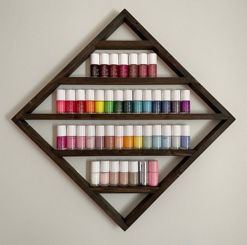 May include: A wooden diamond-shaped shelf with four tiers, displaying a rainbow assortment of nail polish bottles with white caps.