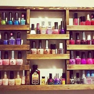 May include: A wooden shelf unit with multiple shelves for storing nail polish bottles. The shelves are filled with various colors of nail polish, including red, pink, purple, blue, green, and clear.