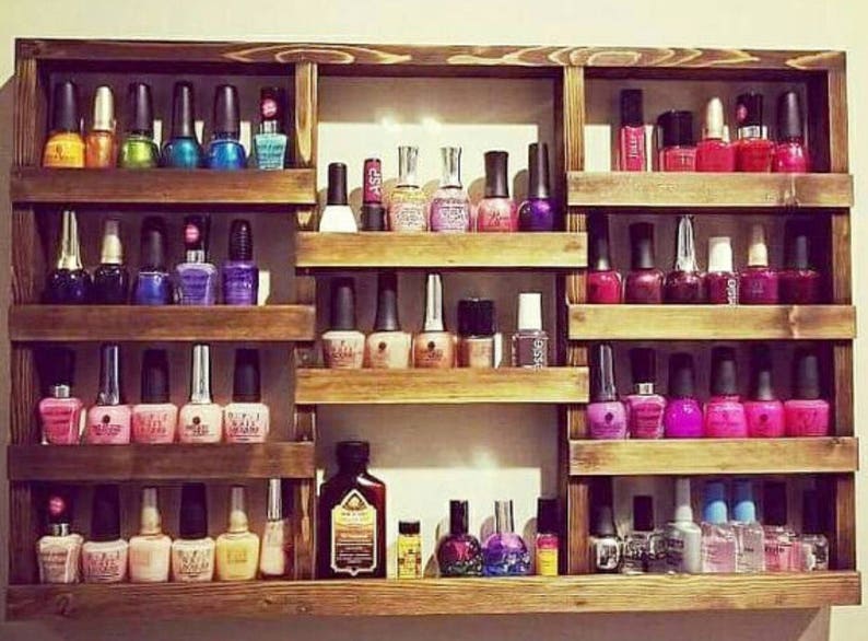 May include: A wooden shelf unit with multiple shelves for storing nail polish bottles. The shelves are filled with various colors of nail polish, including red, pink, purple, blue, green, and clear.