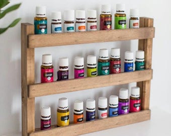 May include: A wooden essential oil shelf with three tiers, holding numerous small glass bottles with white caps and colorful labels. The shelf is made of light brown wood and is displayed against a white background.
