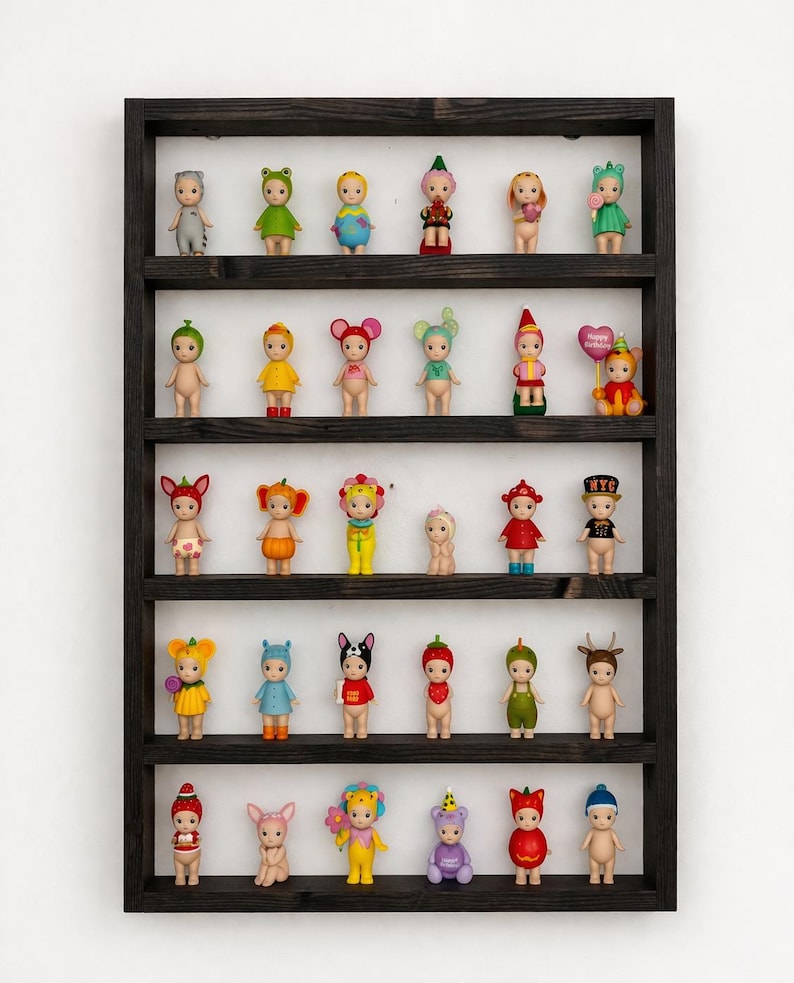 May include: A dark wooden display shelf filled with small, colorful figurines. The figurines are dressed in various outfits, including animal costumes and floral designs. The shelf is mounted on a white wall, creating a clean and organized presentation of the collectibles.