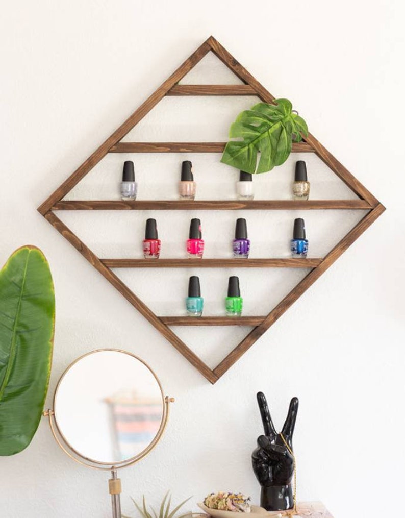 May include: A wooden diamond-shaped shelf with three tiers, holding rows of colourful nail polish bottles. The shelf is mounted on a white wall.