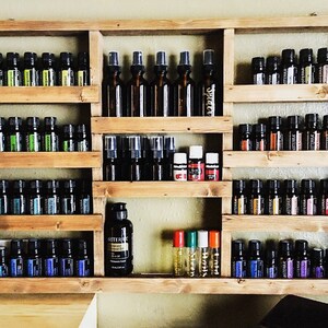 May include: A wooden shelf unit with multiple shelves, each filled with small glass bottles of essential oils. The bottles are arranged in rows and are of various colors, including green, blue, and purple. There are also a few larger bottles with spray tops.