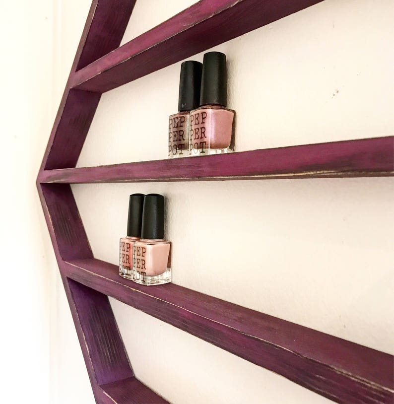May include: Purple hexagonal wooden shelf with three shelves, displaying nail polish bottles. The bottles are clear with black caps and have the text "PEP PER POT" on the labels.