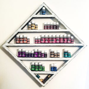May include: White diamond-shaped shelf with multiple tiers holding rows of small glass bottles with colorful liquids. The bottles are arranged in a rainbow pattern.
