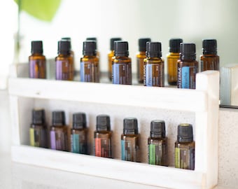 May include: A white wooden shelf with two tiers holds a collection of amber glass bottles with black caps. The bottles are labeled with the word "doterra" and various essential oil names, including "Breathe", "Peppermint", and "On Guard".