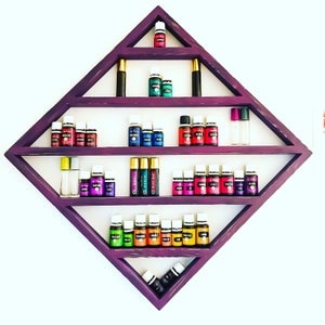 May include: A purple diamond-shaped shelf with five shelves holds rows of small glass bottles with colorful liquids. The bottles are arranged in a grid pattern. The shelf is mounted on a white wall.