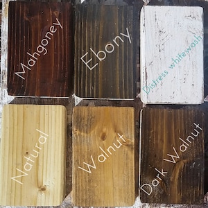 May include: A collection of six wooden blocks showcasing different stain colors. The colors include Mahogany, Ebony, Distress whitewash, Natural, Walnut, and Dark Walnut. Each block has the color name written on it in a cursive font.