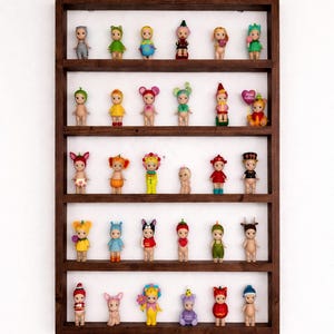 May include: A wooden display shelf filled with small, decorative figurines. The figurines are of various designs, including animals and characters, and are arranged on multiple shelves. The shelf is a dark brown color and is mounted on a white wall.
