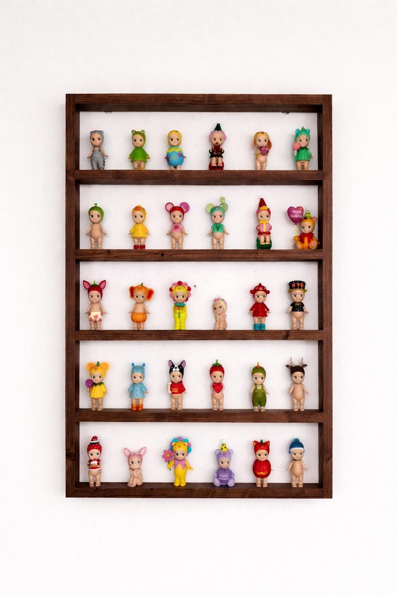 May include: A wooden display shelf filled with small, decorative figurines. The figurines are of various designs, including animals and characters, and are arranged on multiple shelves. The shelf is a dark brown color and is mounted on a white wall.