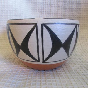 May include: A ceramic bowl featuring a cream-colored upper section decorated with bold, black geometric patterns consisting of triangles and curved shapes, contrasted by a solid terracotta-colored base.