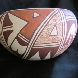 May include: A white ceramic bowl with a geometric design in brown and orange. The bowl has a rounded shape and a smooth surface.