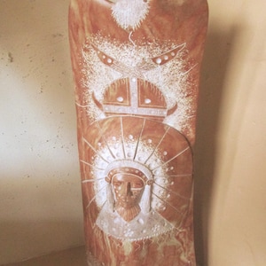 May include: A tall, reddish-brown carved wooden sculpture featuring a Native American figure with a headdress and a butterfly at the base. The sculpture has intricate details and a textured surface, with white accents. The top has a beard and a helmet design.