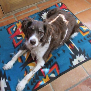 May include: A brown and white dog with a white patch on its back is lying on a blue and red patterned dog bed.