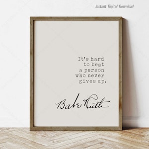 May include: A framed print with a light background and the quote "It's hard to beat a person who never gives up." The signature "Babe Ruth" is below the quote. The frame is brown.