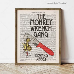 May include: A framed print featuring the title "The Monkey Wrench Gang" in bold black letters, with the author's name, Edward Abbey, below. The artwork includes a red and gray wrench graphic over a vintage book page background.