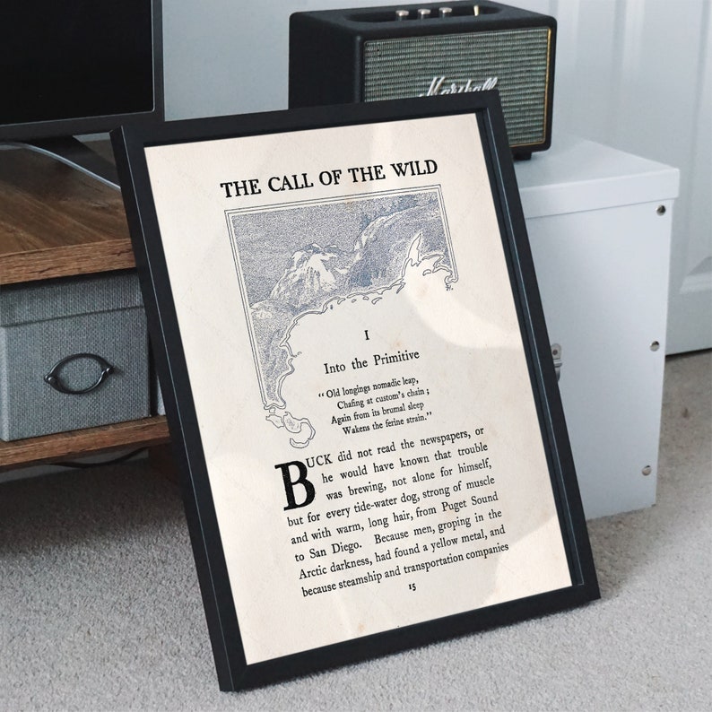 May include: A framed print of a book cover for "The Call of the Wild" by Jack London. The cover features a black and white illustration of a mountain range and a body of water. The text "The Call of the Wild" is printed in black at the top of the cover. The text "Into the Primitive" is printed in black below the illustration. The text "Old longings nomadic leap, Chafing at custom's chain: Again from its brumal sleep Wakens the ferine strain." is printed in black below the text "Into the Primitive". The text "BUCK did not read the newspapers, or he would have known that trouble was brewing, not alone for himself, but for every tide-water dog, strong of muscle and with warm, long hair, from Puget Sound to San Diego. Because men, groping in the Arctic darkness, had found a yellow metal, and because steamship and transportation companies" is printed in black below the text "Wakens the ferine strain."