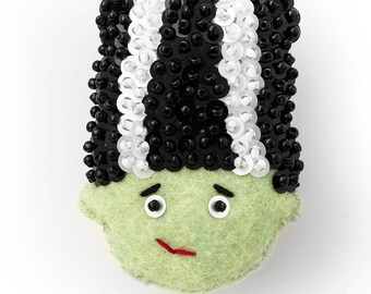 May include: A green felt Frankenstein monster with black and white sequin hair. The monster has black eyes and a red stitched mouth.