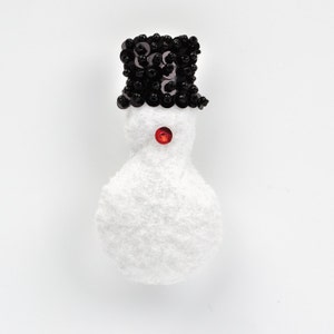 May include: A white snowman ornament with a black sequined top hat and a red button nose.
