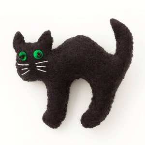 Pode incluir: Um brinquedo de gato de feltro preto com olhos verdes. O gato está em posição de agachamento com o rabo enroscado.