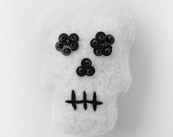 May include: White felt skull with black sequin eyes and a stitched mouth.