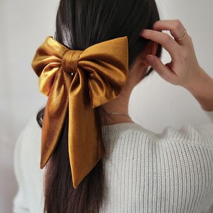 May include: A large, golden brown velvet bow is tied in a ponytail. The bow is tied with a long, flowing tail.