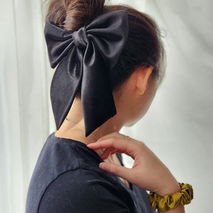 May include: A black satin hair bow tied in a large bow shape, worn in a woman's hair.