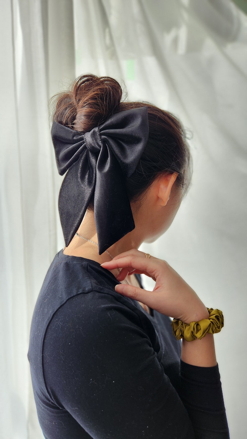 May include: A black satin hair bow tied in a large bow shape, worn in a woman's hair.
