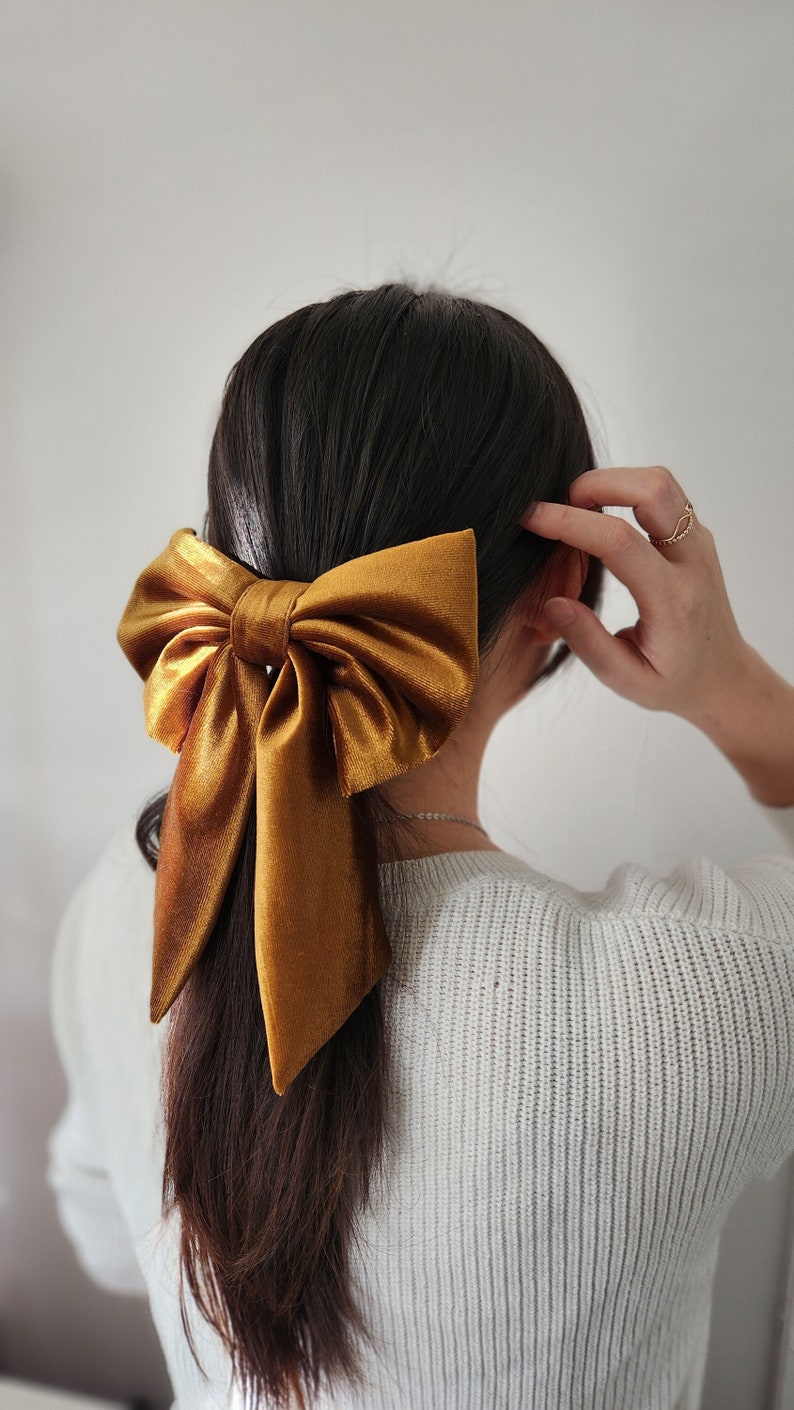May include: A large, golden brown velvet bow is tied in a ponytail. The bow is tied with a long, flowing tail.