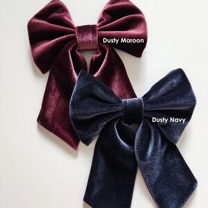 May include: Two velvet hair bows, one dusty maroon and one dusty navy. The bows are tied in a large, loose knot and have long tails.