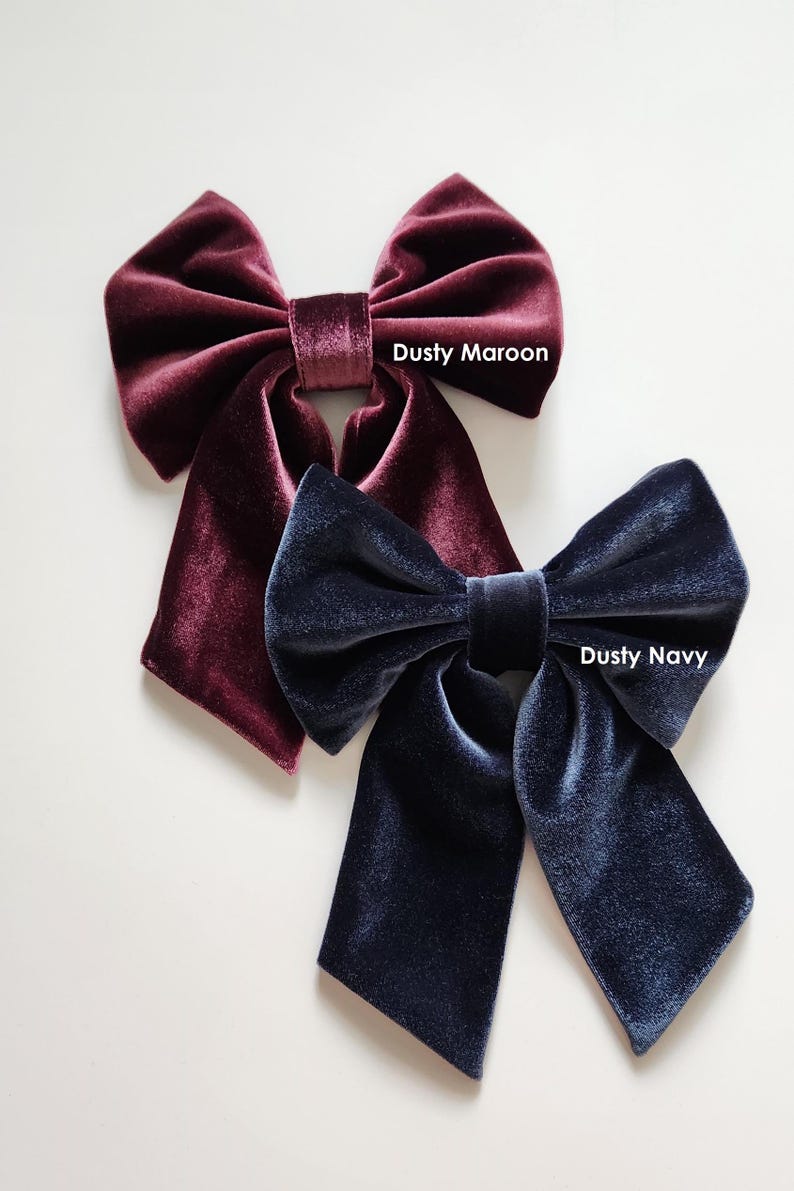May include: Two velvet hair bows, one dusty maroon and one dusty navy. The bows are tied in a large, loose knot and have long tails.