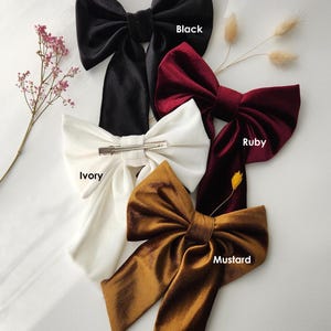 May include: Four velvet hair bows in different colors: black, ruby red, ivory, and mustard yellow. Each bow has a metal clip for attaching to hair.