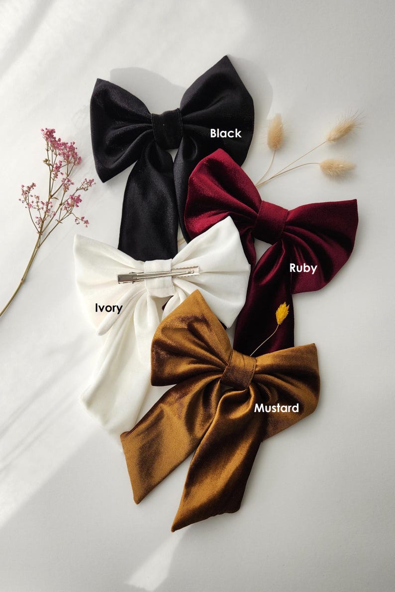May include: Four velvet hair bows in different colors: black, ruby red, ivory, and mustard yellow. Each bow has a metal clip for attaching to hair.
