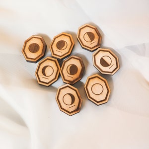 Op de afbeelding: Acht achtekante houten maanfase-tokens met een lichtbruine houtkleur. Elk token heeft een andere fase van de maan in zwart.