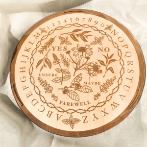 May include: A wooden Ouija board with a floral design and the words "YES", "NO", "UNSURE", "MAYBE", and "FAREWELL" inscribed on it.