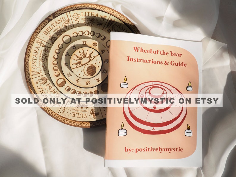 May include: A pink booklet with the title "Wheel of the Year Instructions & Guide" and the text "SOLD ONLY AT POSITIVELYMYSTIC ON ETSY" and "by: positivelymystic". The booklet features a red and white illustration of a wheel with concentric circles.