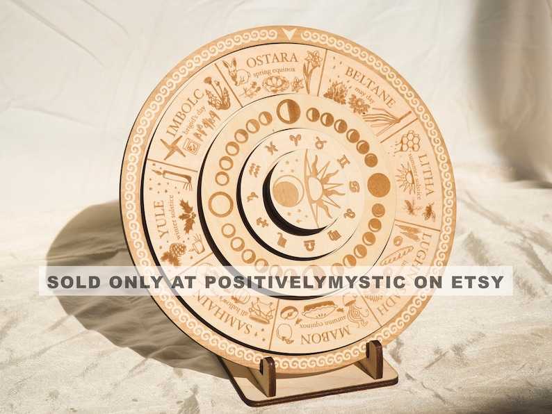 May include: A wooden wheel with a circular design, featuring the names of the eight sabbats of the Wheel of the Year, including Yule, Imbolc, Ostara, Beltane, Litha, Lughnasadh, Mabon, and Samhain. The wheel also includes a moon phase tracker and a sun and moon symbol.