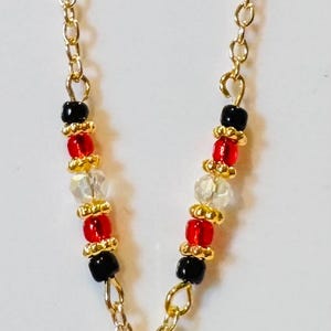 Puede incluir: Un collar de cadena dorada con un colgante de Mickey Mouse. La cadena presenta cuentas negras, rojas y transparentes. El colgante es una cabeza de Mickey Mouse negra y roja con detalles de cristal.