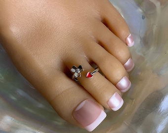 May include: Silver toe ring with a flower design and a red heart charm.