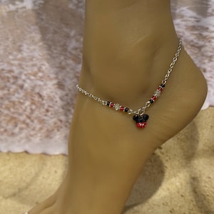 Pode incluir: Tornozeleira prateada com um pingente do Mickey Mouse. A tornozeleira apresenta uma corrente com contas vermelhas, pretas e transparentes. O pingente do Mickey Mouse &eacute; vermelho e preto. A tornozeleira &eacute; usada em um tornozelo.