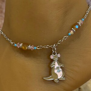 May include: Silver anklet with a kangaroo charm. The anklet features a delicate chain with pink, blue, and amber-colored beads. The kangaroo charm is silver with pink and brown accents.