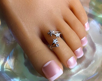 May include: Silver toe ring with three white flower accents and a single clear rhinestone.