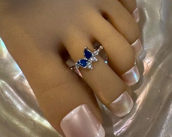 May include: A silver toe ring with a butterfly design featuring blue and clear gemstones.