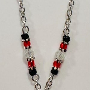 Pode incluir: Colar de corrente prateada com um pingente do Mickey Mouse. O pingente &eacute; preto e vermelho com detalhes de cristal. A corrente tem contas pretas, vermelhas e transparentes.