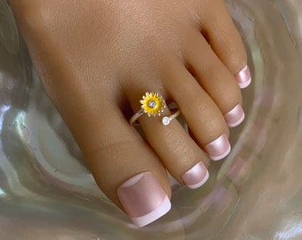 May include: A silver toe ring with a yellow enamel sunflower design and a clear rhinestone accent.