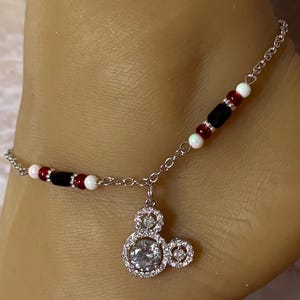 Puede incluir: Tobillera plateada con un dije de Mickey Mouse con una piedra central grande y transparente y piedras m&aacute;s peque&ntilde;as alrededor. La cadena est&aacute; adornada con cuentas rojas, negras y blancas. Un accesorio divertido.