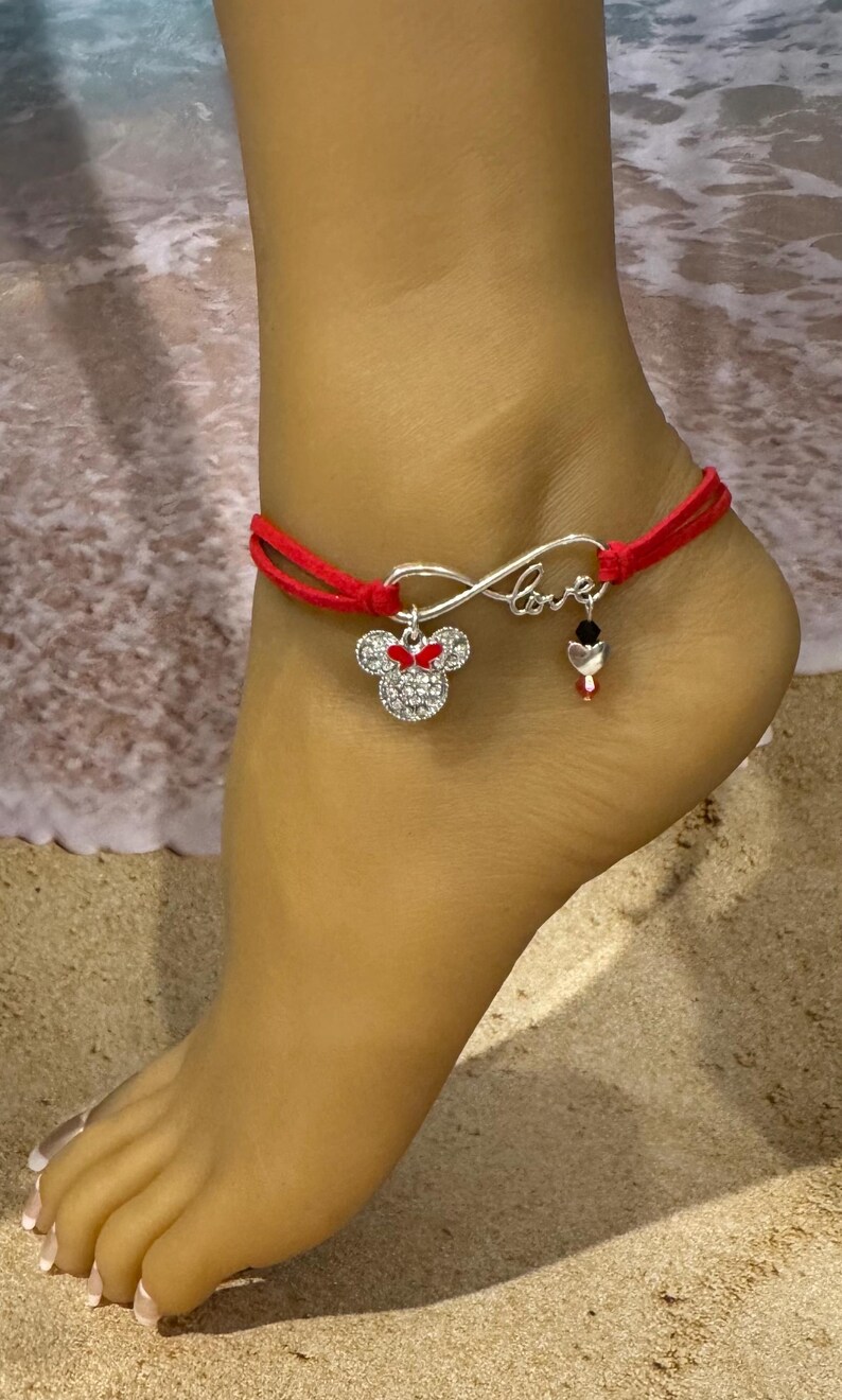 May include: Red ankle bracelet with an infinity symbol charm and a Minnie Mouse charm. The charm is silver with red accents and rhinestones.