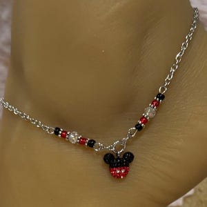 Pode incluir: Tornozeleira prateada com um pingente do Mickey Mouse. O pingente &eacute; vermelho e preto com detalhes em cristal. A corrente &eacute; adornada com contas vermelhas, pretas e transparentes. Um acess&oacute;rio delicado e divertido.