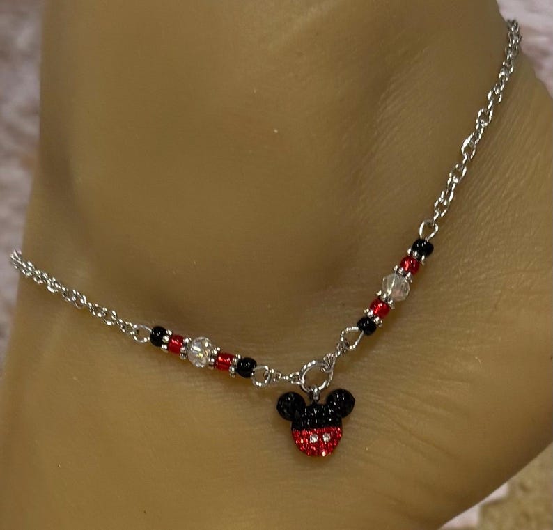 Pode incluir: Tornozeleira prateada com um pingente do Mickey Mouse. O pingente &eacute; vermelho e preto com detalhes em cristal. A corrente &eacute; adornada com contas vermelhas, pretas e transparentes. Um acess&oacute;rio delicado e divertido.